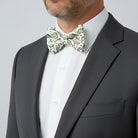 Man wearing a green dinosaur bowtie and dark gray suit with a white shirt on a light gray background
