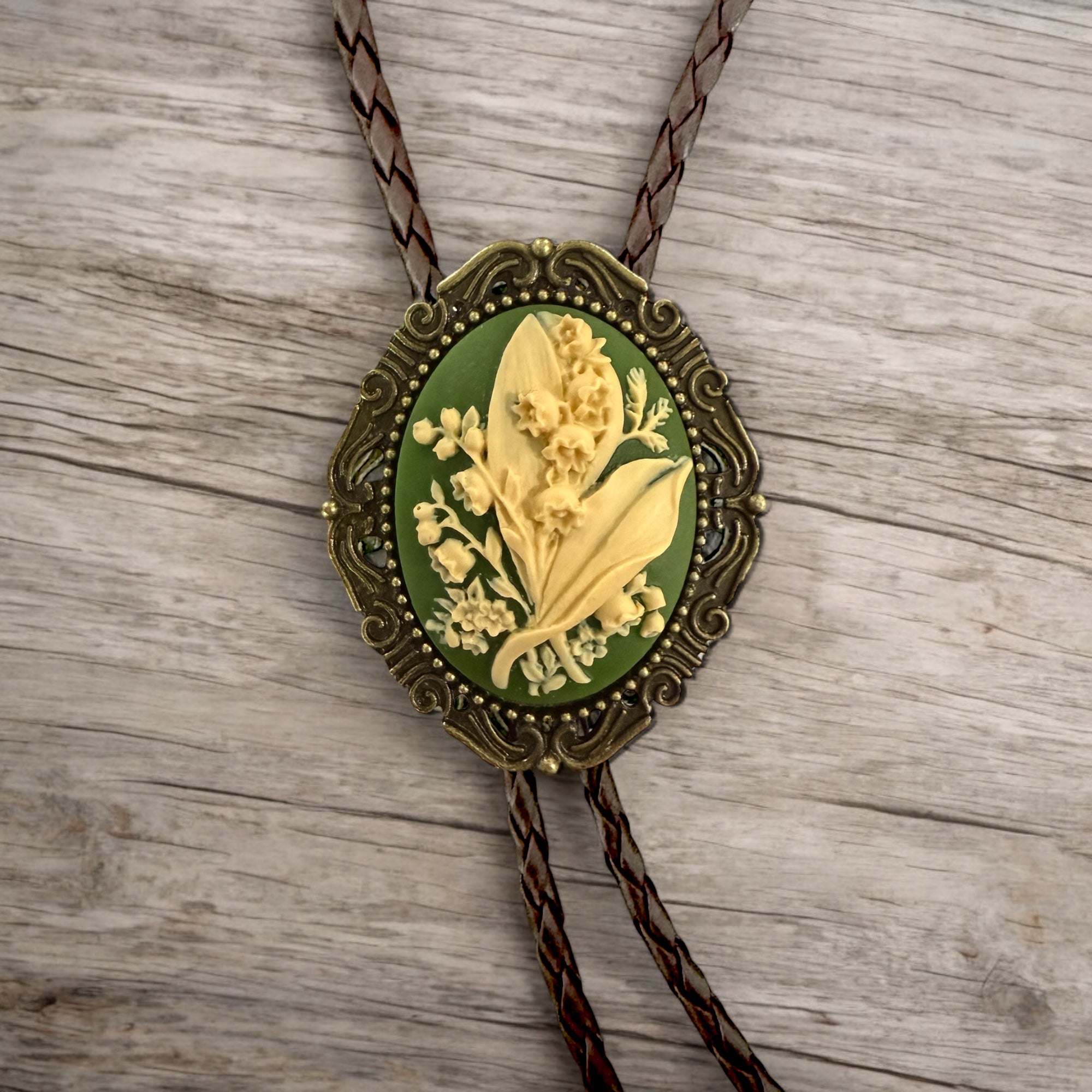 Bolo tie with green lily of the valley floral design on a wooden surface