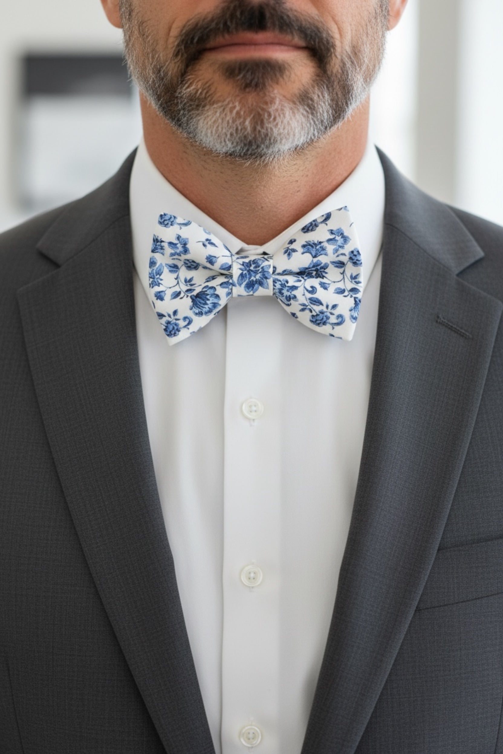 Groomsman wearing a gray suit with a blue and white floral bow tie at a wedding.
