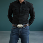 Person wearing a black shirt and blue jeans with a decorative gorilla cowboy belt on a dark background
