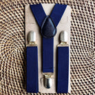 Set of blue suspenders with silver clips on a cardboard backing, placed on a woven surface.