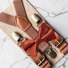 A pair of brown suspenders with a red bow tie attached, displayed on a marble surface.