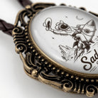 A close-up image of a decorative pendant featuring a black and white illustration of a person riding a rocket ship, with stars and a crescent moon in the background.