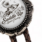 A close-up of a decorative metal object with a cowboy riding a rocket ship and the text "Saddle Cowboy" on it.