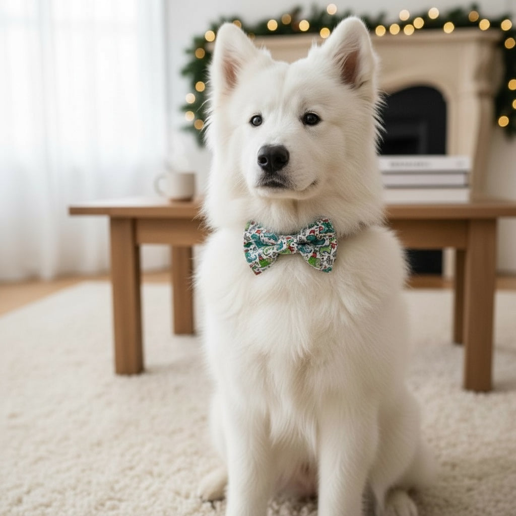 White dog wearing a Dinosaur Christmas dog bow tie sitting in a cozy room with a fireplace and Christmas decorations.