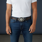 Person wearing blue jeans and a white t-shirt with a dark belt and silver raccoon belt buckle against a gray background