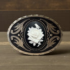 Decorative floral belt buckle with a white rose design on a wooden surface