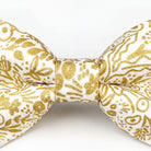 A close-up view of a gold and white bow tie with a floral pattern.