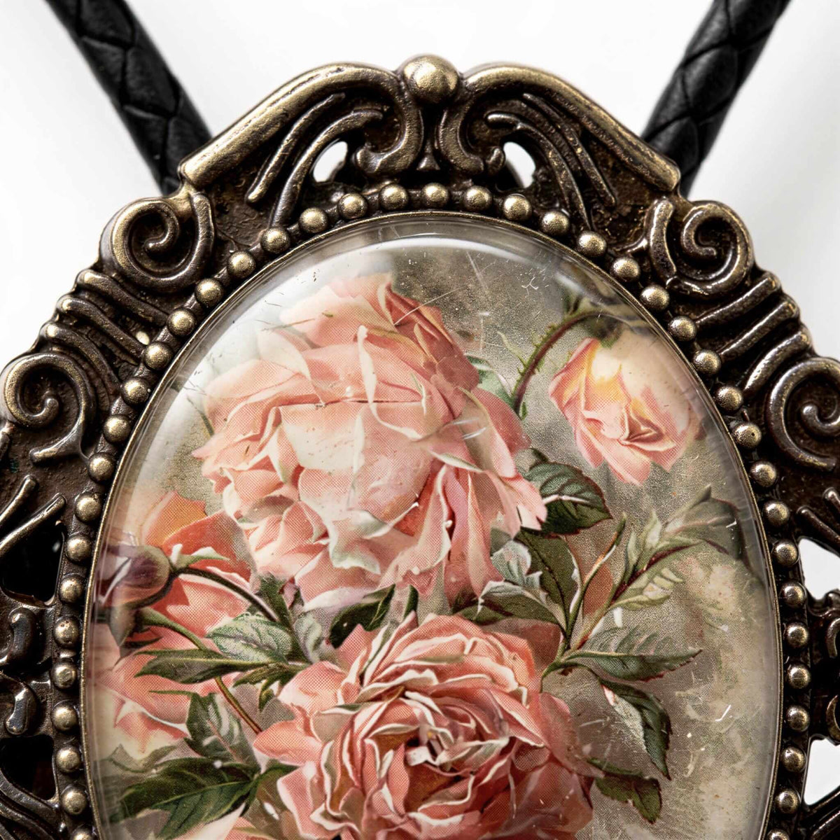 A close-up image of a decorative bolero tie featuring a floral design with pink roses and green leaves.