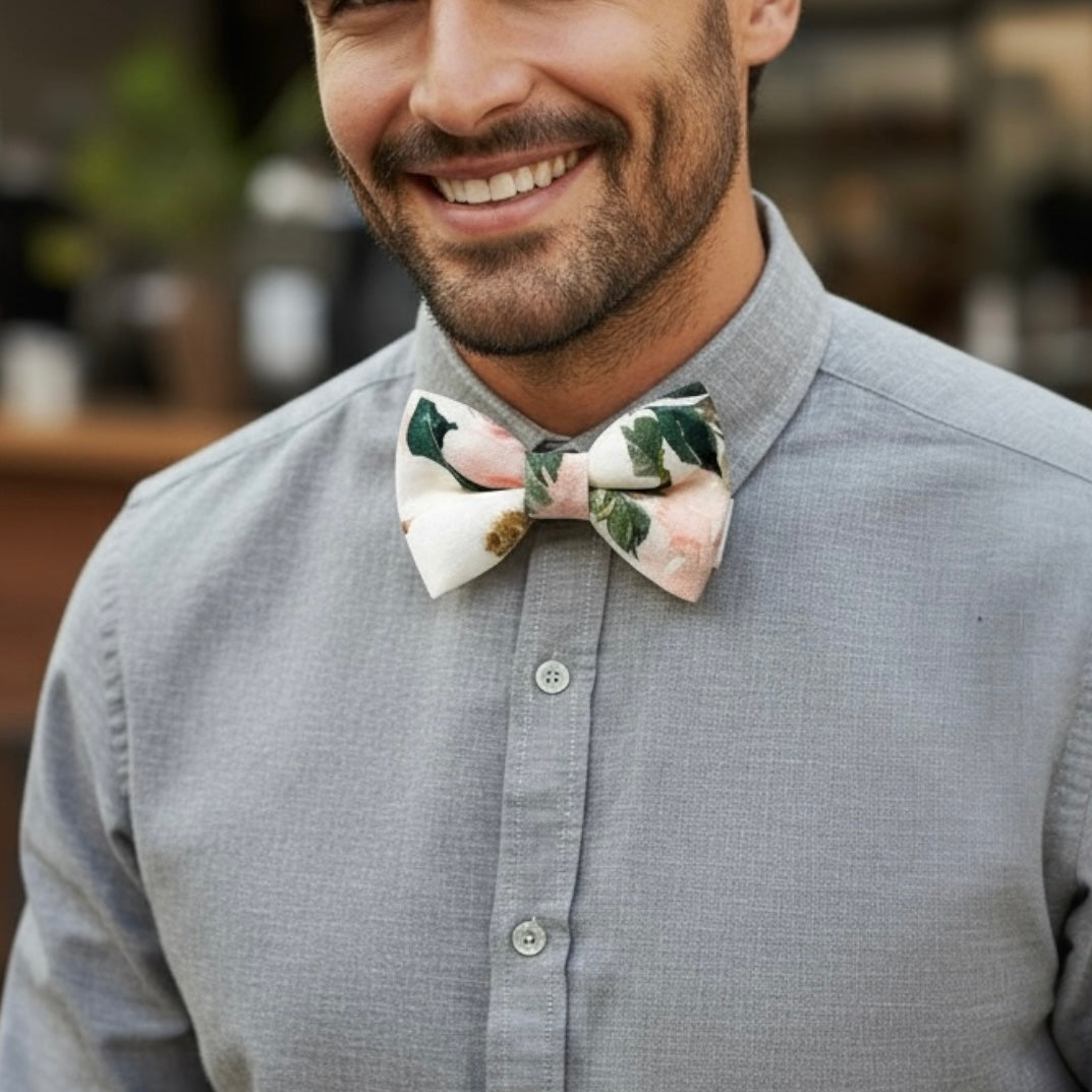 Groomsman wearing a gray shirt with a blush floral bow tie, smiling outdoors.