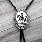 Black and white Cowboy Bolo tie with a decorative pendant featuring a horse and rider on a wooden surface