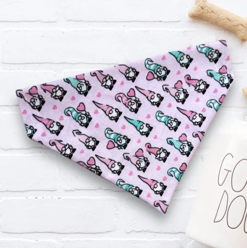 Valentines Day Dog bandana with light pink gnomes on a white surface with dog treats and a 'Good Dog' mug.