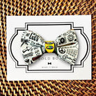 A colorful bow tie with various doodles and text printed on it, displayed on a white card with a wicker border.