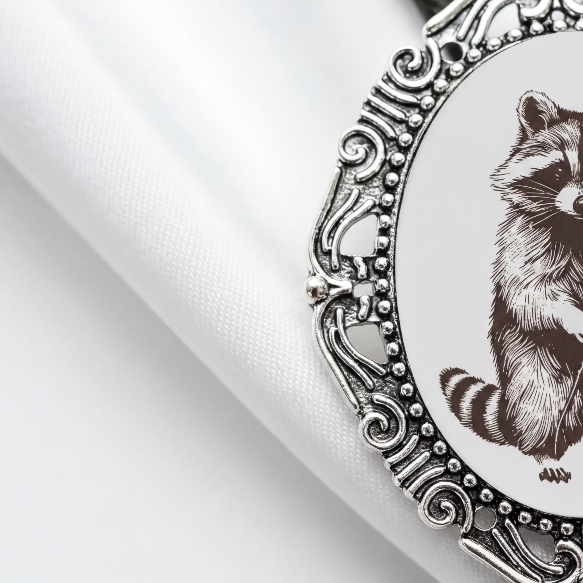 a close-up view of a decorative metal frame with a raccoon illustration on it, placed on a white fabric surface.