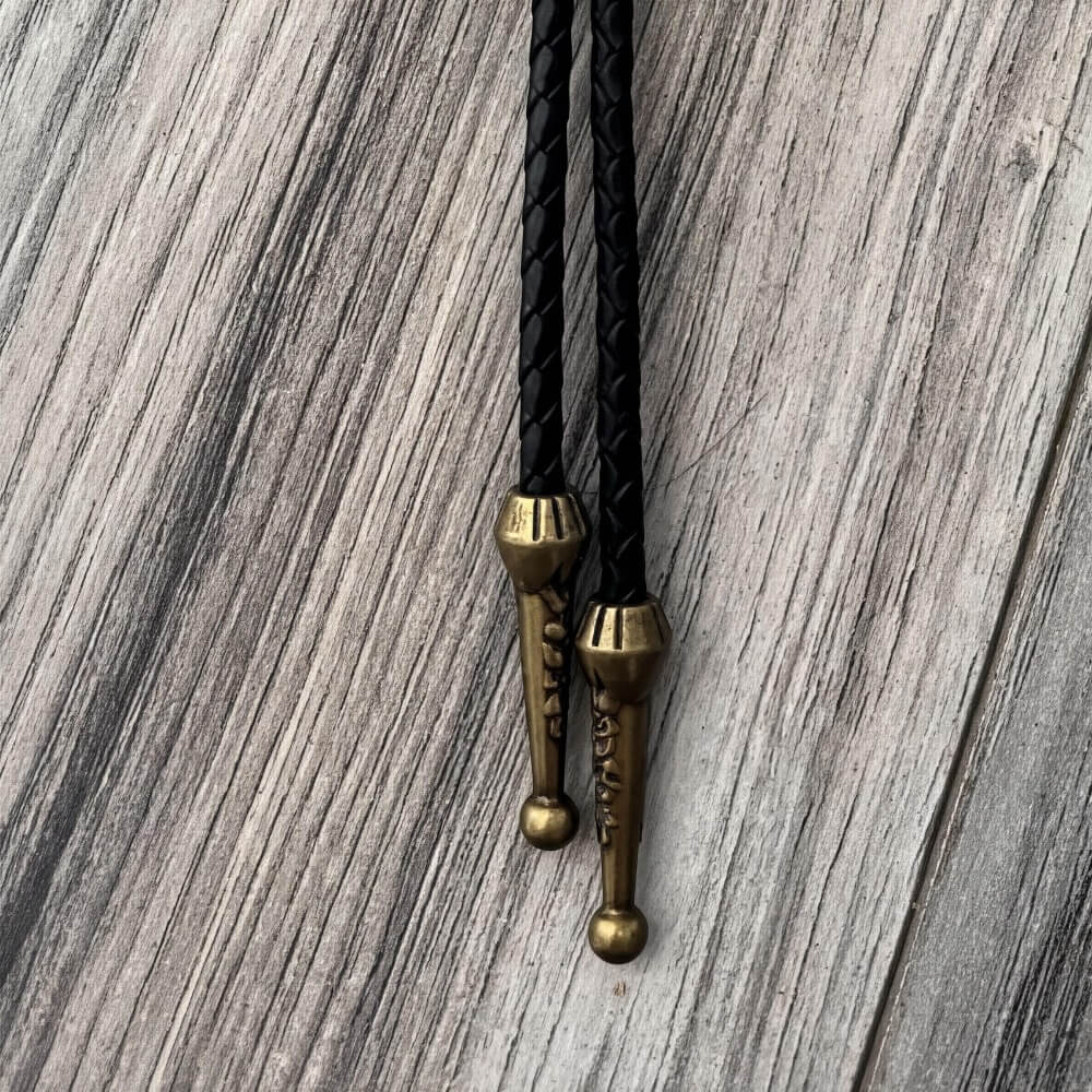 a close-up view of a black leather tie with brass-colored metal ends, resting on a wooden surface.
