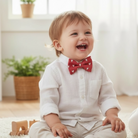 Child wearing a red Valentine’s Day bow tie with white heart patterns, sitting indoors.