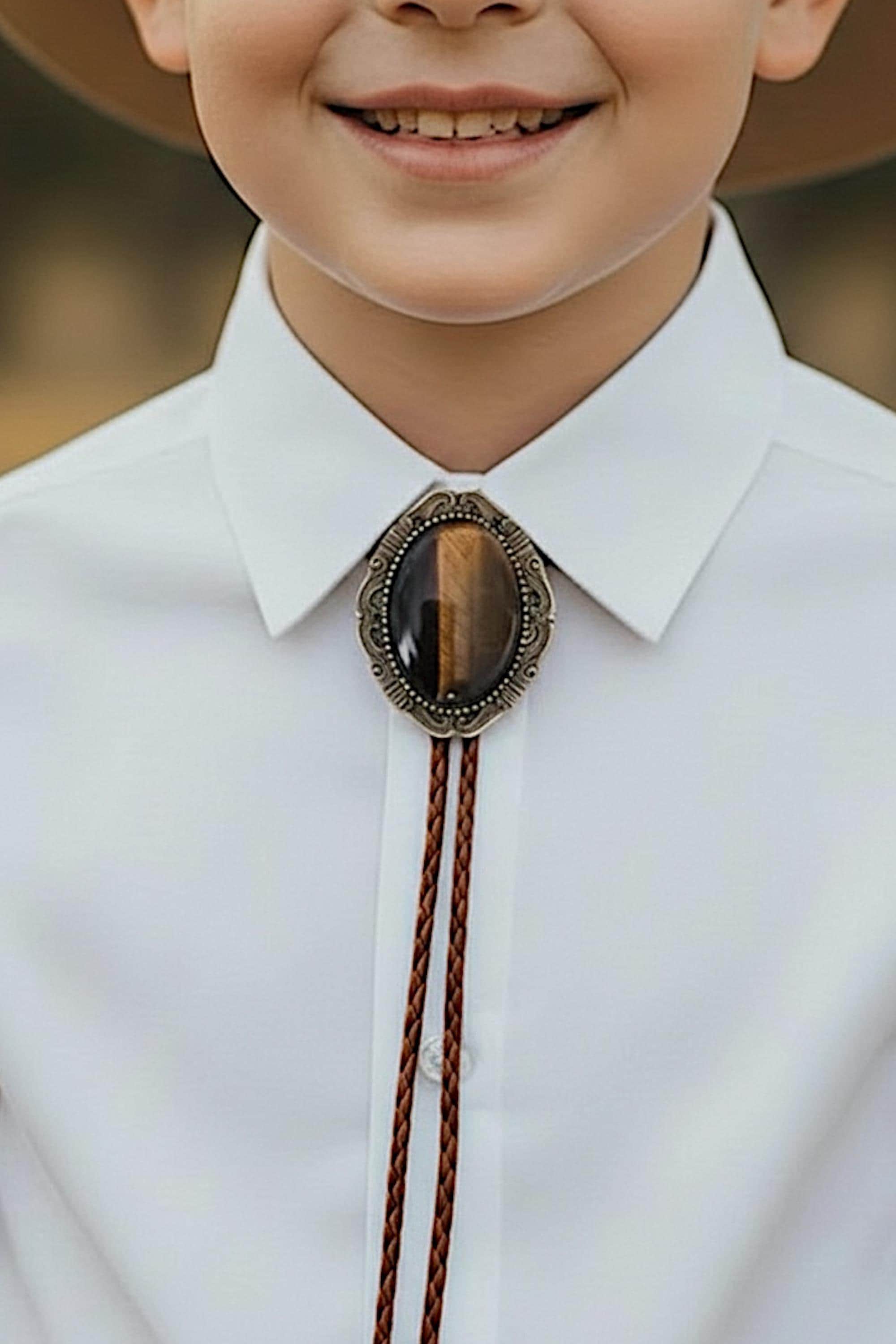 A young boy wearing a white collared shirt and a decorative tie with a large oval-shaped stone or gemstone.