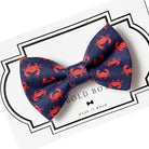 Navy blue dog bow tie with red crab pattern on a white background with 'The Bold Bow Tie' branding.