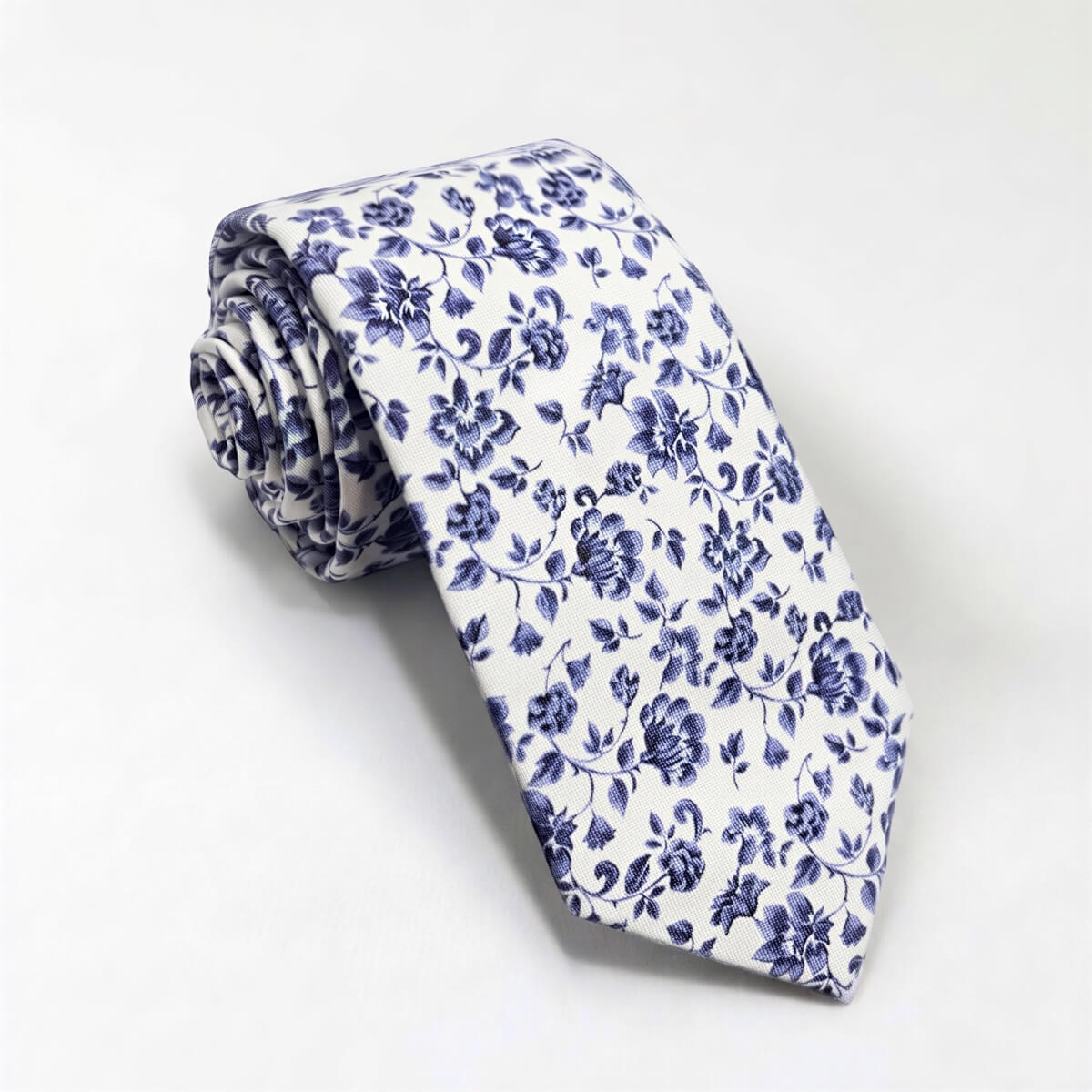 A white and blue floral print tie is rolled up and displayed against a white background.