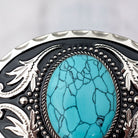 A close-up image of a decorative black and silver belt buckle with a large turquoise stone in the center.