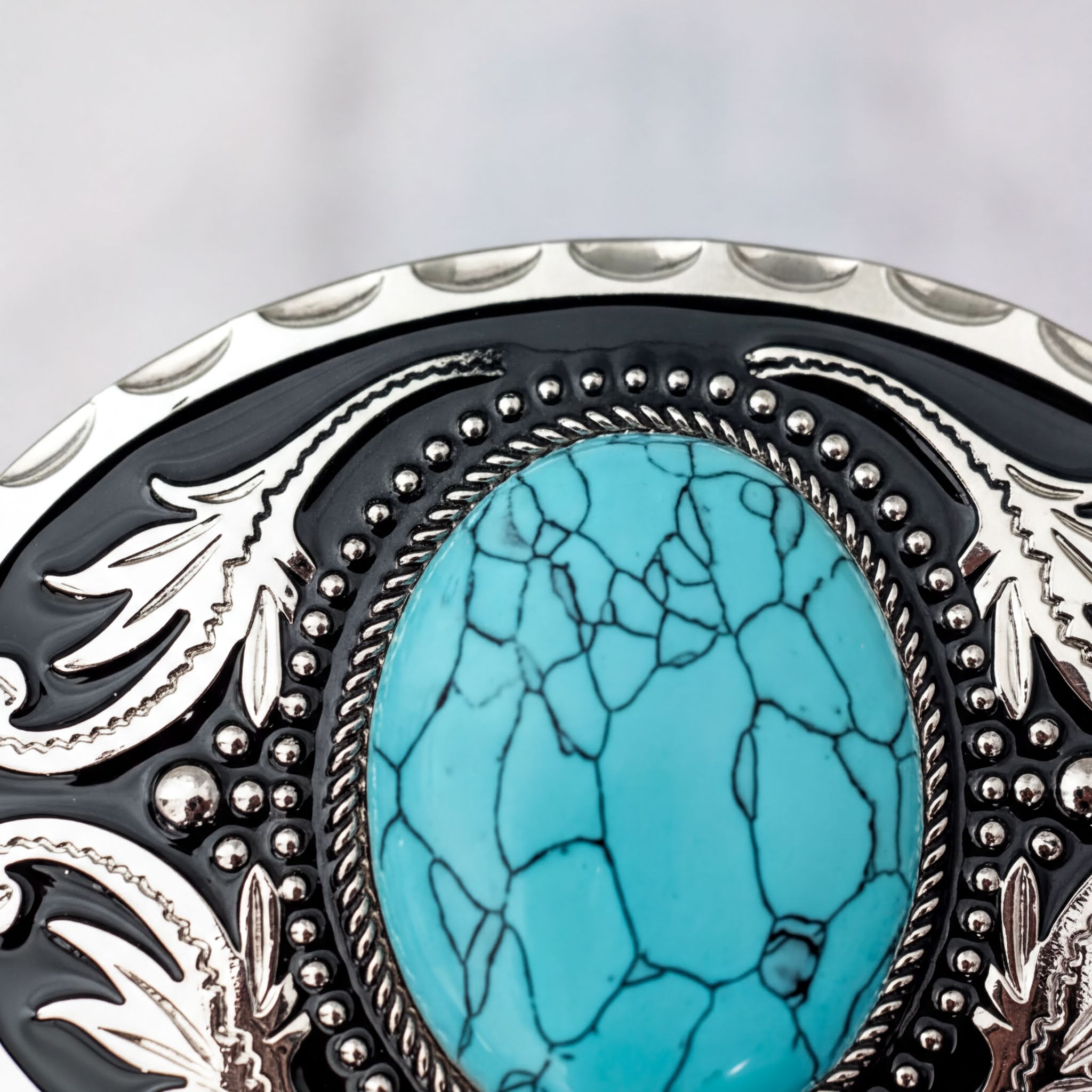 A close-up image of a decorative black and silver belt buckle with a large turquoise stone in the center.