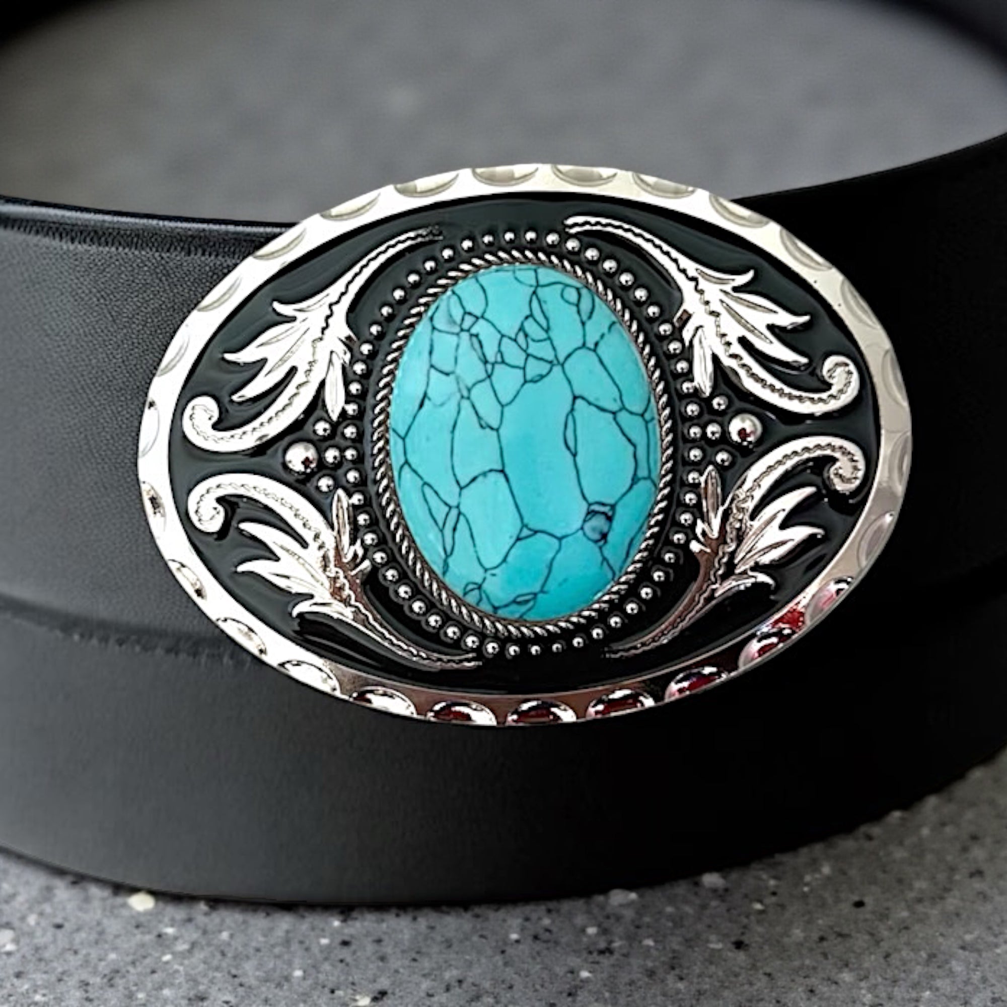 Black belt with a decorative turquoise belt buckle featuring a turquoise stone and silver detailing on a dark background.