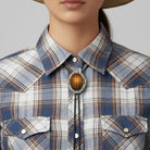 Cowgirl wearing a plaid shirt with a Christian cross bolo tie and straw hat on a plain background