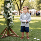Child in dinosaur bowtie standing next to a floral arrangement at a wedding.
