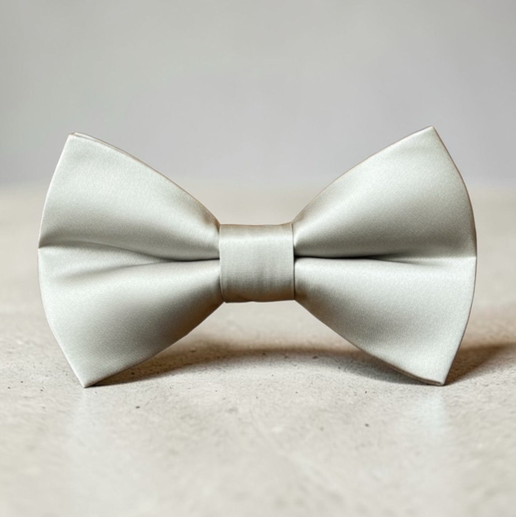 Silver bow tie for men and boys for weddings, groomsmen ties and ring bearers, on a beige surface with a light gray background