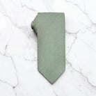 A sage green tie for men’s wedding necktie with a matching fabric neck loop, laid flat on a textured white surface.