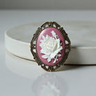 Decorative brooch with a white rose design on a pink background, set against a light gray background.