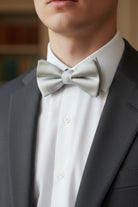 Man wearing a silver bow tie and gray suit jacket at a wedding.