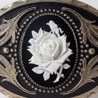 a close-up view of a decorative piece with a black background and a white rose as the central element. The rose is surrounded by intricate metalwork and patterns, creating a visually striking and elegant design.
