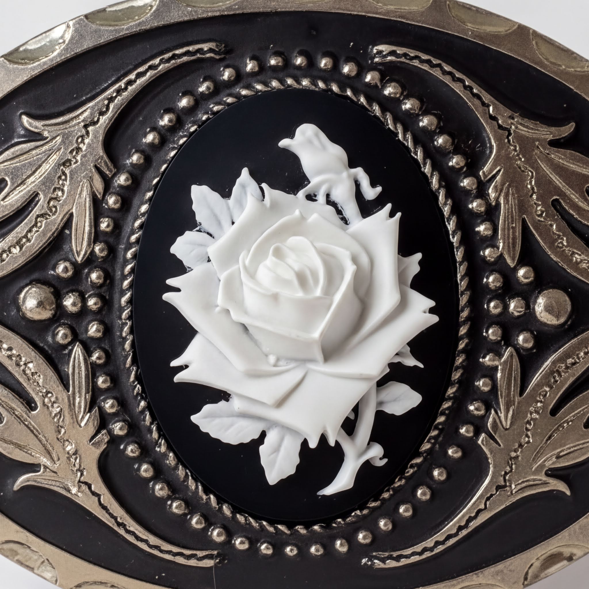 a close-up view of a decorative piece with a black background and a white rose as the central element. The rose is surrounded by intricate metalwork and patterns, creating a visually striking and elegant design.