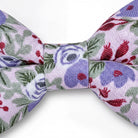 A close-up view of a bow tie with a floral pattern in shades of purple, green, and red.
