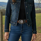 Person wearing a denim jacket and jeans with a cat belt buckle in a field