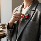 Person wearing a gray blazer with a red rose brooch, pointing at it.