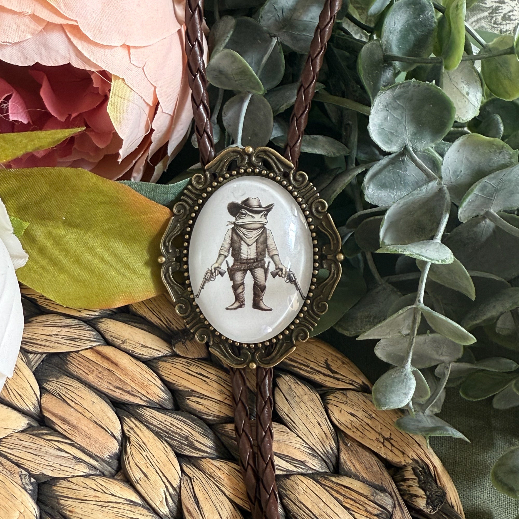 Bolo tie with frog cowboy pendant on woven mat and floral background