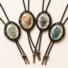 Wedding floral bolo ties with vintage bronze frames, braided leather cords, and botanical flower designs for groom and groomsmen western wedding attire.