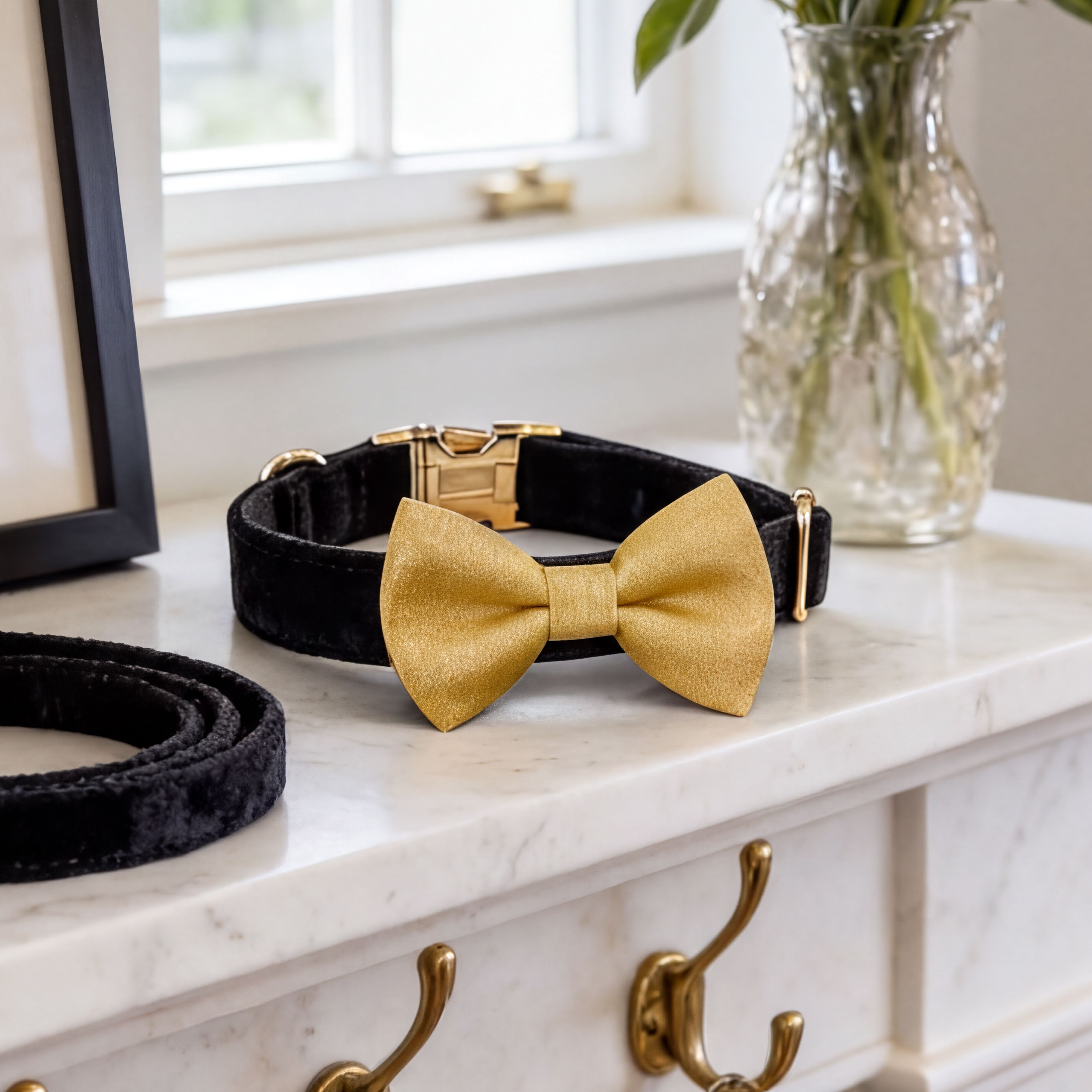 a gold bow tie, a black velvet collar, and a black belt on a white marble countertop.