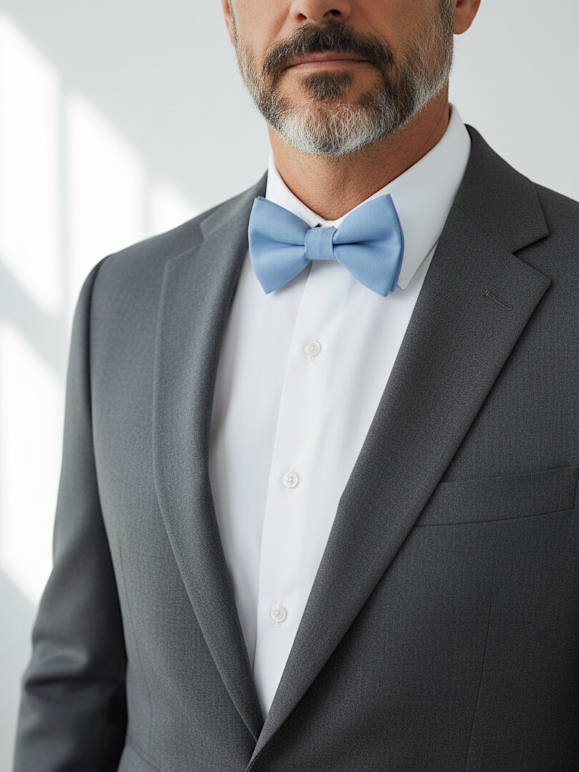 Groomsman wearing a gray suit and a dusty blue bow tie in a wedding with a white shirt and blue bow tie.