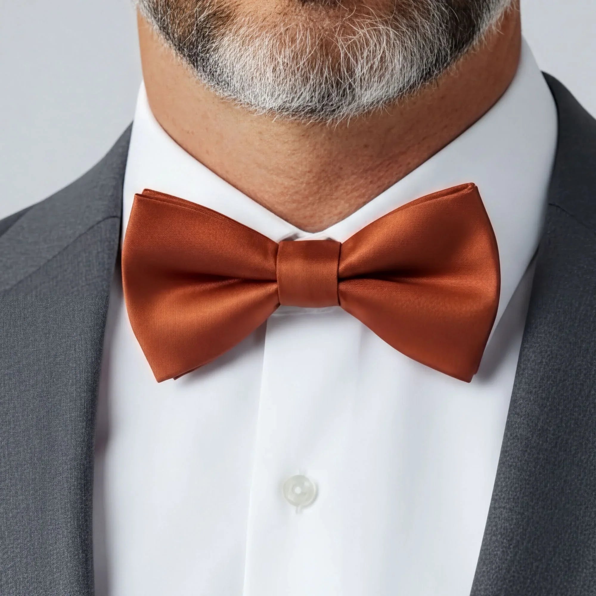 A close-up of a man's neck and chest area, focusing on a brown bow tie and a gray suit jacket.