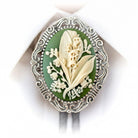 A decorative oval-shaped brooch with a floral design, featuring white flowers and leaves against a green background.