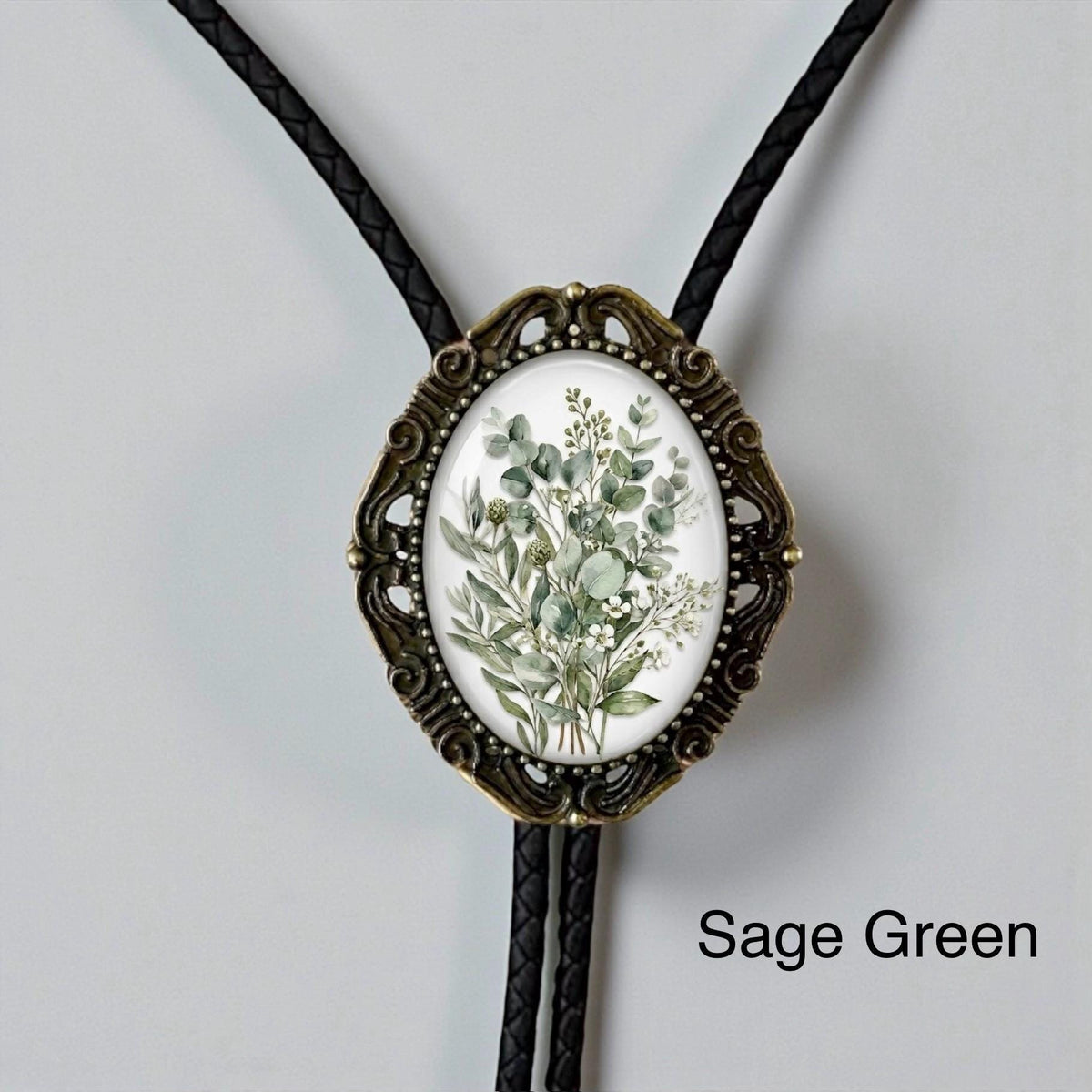 Sage green floral bolo tie with vintage bronze oval frame, braided leather cord, and soft botanical greenery design for groom, groomsmen, rustic weddings, western wedding attire, and handmade formal accessories.