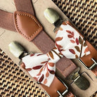 Brown suspenders with terracotta floral patterned clips on a woven surface