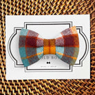 Product graphic showcasing the back of a pre-tied bow tie in a red and black buffalo plaid pattern, resting on a rustic wood surface. Two black elastic loops are attached to the center knot to slide onto a pet collar. Overlay text reads: Back of Bow Tie (may not be actual bow tie in listing).