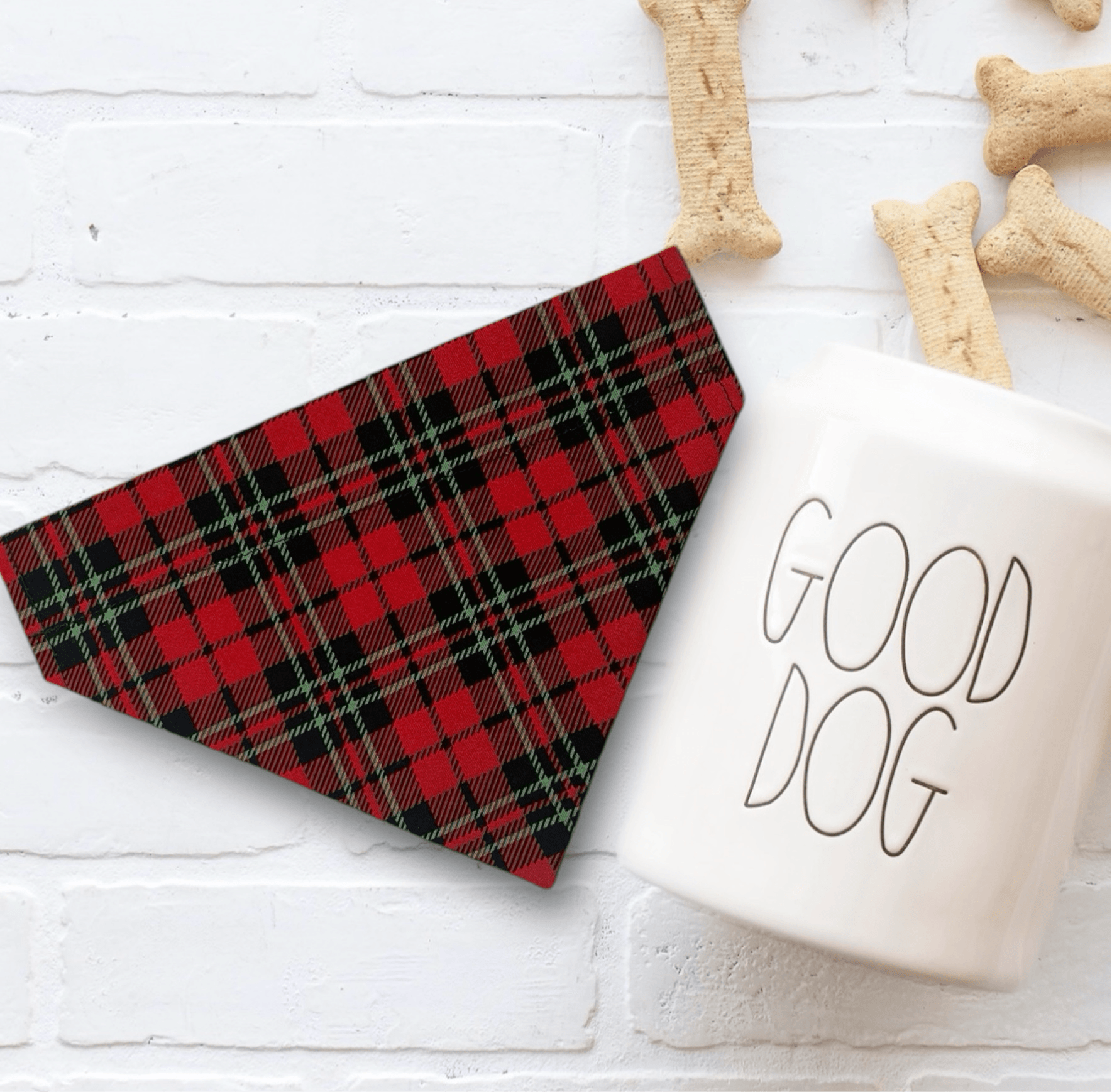 Red plaid Christmas dog bandana and 'Good Dog' mug on a white surface with dog bones.