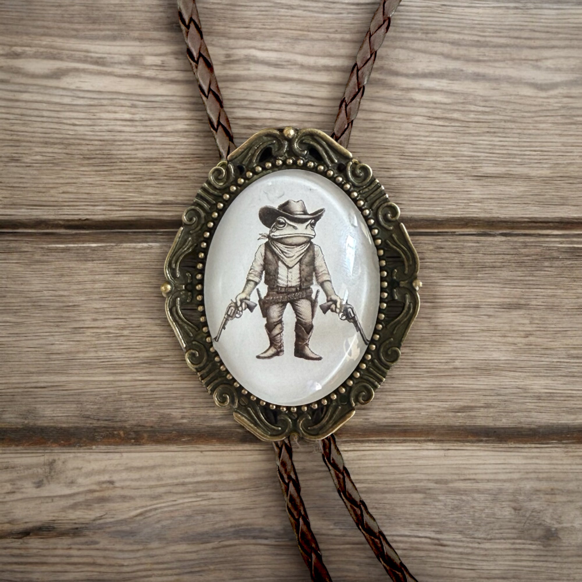Bolo tie with frog cowboy design on a wooden surface