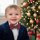 Christmas bow tie worn by a toddler by a Christmas tree.