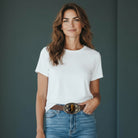 Woman wearing a white t-shirt and blue jeans with a tiger’s eye belt buckle against a dark background